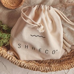 A beige cotton drawstring bag with the text "SHAECO" printed on it. The bag appears to be a simple, minimalist design suitable for weekend use or as a reusable shopping bag.