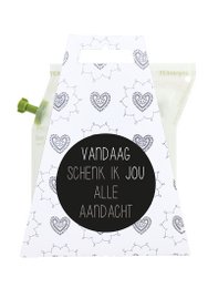 A white tea towel with a black text that says "Vaddag's Spekkie in jou alle Handoek" and a pattern of heart shapes. The image also shows various tea ingredients such as cinnamon sticks, an apple, and a honey jar.