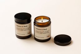 Cashmere & Musk scented candle, round glass jar with black lid, warm amber-colored wax, floral and musky fragrance.