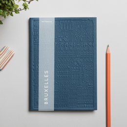A hardcover notebook with a textured cover in various colors, including blue, yellow, rust, green, concrete, and lavender. The notebook is titled "The Brussels Notebook" and appears to be a product for a stationery or office supplies brand.