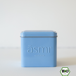 Relaxing massage oil set in a blue tin container with the Asmi logo. The oil bottle has a black cap and label with the Asmi logo.