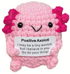  A pink plush toy in the shape of an axolotl with a positive message. The axolotl has a smiling face and is holding a sign that says "I may be a tiny axolotl, but I believe in you... So do your thing!"