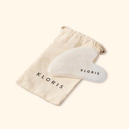  A natural stone Gua Sha tool in a soft fabric pouch, designed for skin care and facial massage. The tool has a smooth, rounded shape and is made of a natural stone material.