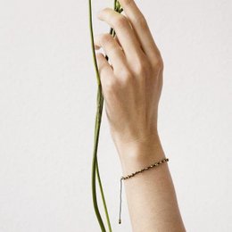 Beaded bracelet with adjustable cord, featuring small beads in a neutral color palette.