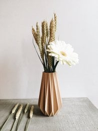 Origami-inspired vase in natural wood, available in 15 cm and 20 cm heights, featuring a minimalist design and a bouquet of dried wheat stalks and a white flower.