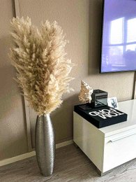 Dried pampas grass in a tall silver vase, with a modern black and white decor piece in the background.