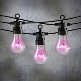 Pink LED light bulbs on a black cord, spelling out the word "Love". The bulbs have a warm, glowing pink light.