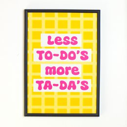 A vibrant yellow poster with the text "Less To-Do's, More Ta-Da's" printed in a bold, playful font. The poster is designed to inspire and motivate, encouraging the viewer to focus on their accomplishments rather than their to-do lists.