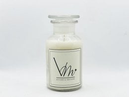 A tall, round white candle in a glass jar with a label that says "Vhr". The candle has a light, creamy color and appears to be a scented candle.