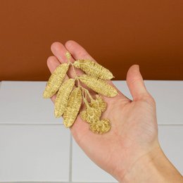 Embroidered brooch with eucalyptus flower design, made of gold-colored thread, featuring a delicate and intricate floral pattern.