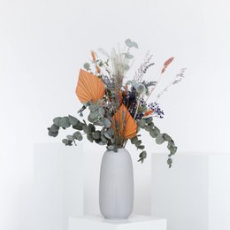 Dried flower bouquet with orange thistles and greenery in a white vase.