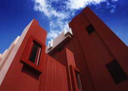 Vibrant red modern architectural building with geometric shapes and patterns against a blue sky with clouds.