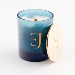 Tall, round scented candle in a blue and navy glass container with a gold letter 'J' embossed on the front. The candle is made of cedar and amber jasmine fragrances.