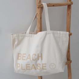  Beige canvas beach bag with the text "BEACH PLEASE" printed on it. The bag has two handles and appears to be a casual, lightweight tote bag suitable for carrying items to the beach or for everyday use.