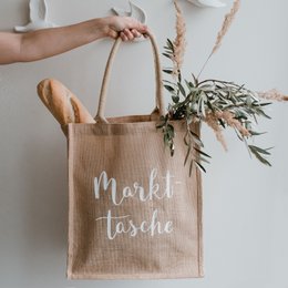 Reusable market bag made of natural jute material, featuring the text "Market Tasche" printed in white lettering.