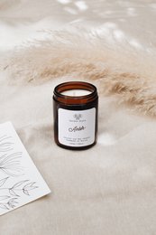 Amber-colored candle in a glass jar with a black label. The candle has a warm, earthy scent and is available in multiple sizes.
