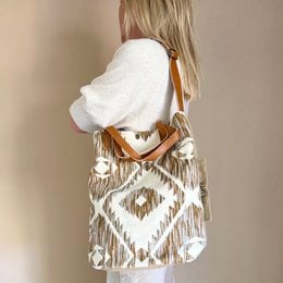 Beige bucket bag with Aztec-inspired pattern, worn with a tan cardigan, denim shorts, and strappy sandals.