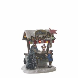 A miniature Christmas village scene made of multi-colored plastic, featuring a small house, trees, and figures. The scene has a whimsical, festive appearance.