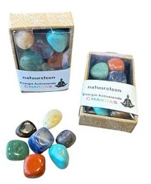 Colorful chakra stones in a wooden box, including red, blue, purple, and green stones. The stones appear to be polished and natural in shape.