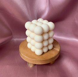 Ivory-colored pillar candle with a cube-like shape, made of wax and resting on a wooden base.