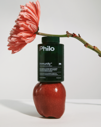 Philo Immunity supplement in a red apple-shaped bottle with a vibrant pink flower. Provides immune system support.