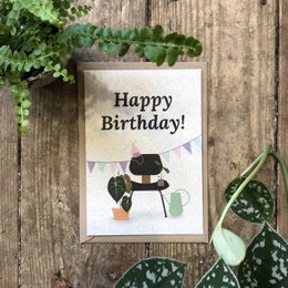 Colorful birthday card with a happy birthday message and a cute cartoon character. The card is framed by a wooden background and surrounded by green leaves, creating a natural and festive atmosphere.