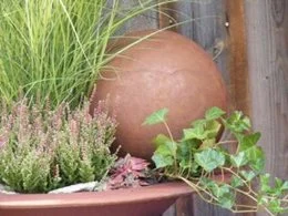 Rusty metal decoration ball with patina finish, available in 3 sizes for garden decor. Spherical shape, textured surface, complemented by surrounding plants.