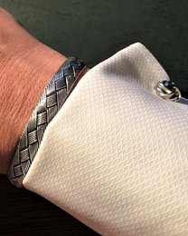 Silver-toned bangle with a woven pattern and a decorative charm.