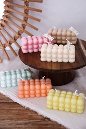  Colorful, round pillar candles in various pastel shades including pink, yellow, orange, mint, and beige. The candles are arranged on a wooden display stand.