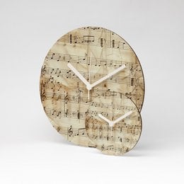 A round wall clock with a vintage sheet music design, measuring 13cm in diameter. The clock features a multicolored design and is made of MDF material.