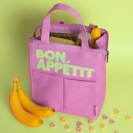 A purple insulated lunch bag with the text "BON APPETIT" printed on it. The bag has two handles and appears to be made of a durable, water-resistant material. The bag is shown alongside some fresh produce, including a banana, suggesting it is designed for carrying food and keeping it fresh.