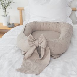 Soft, cozy linen babynest in a variety of colors including sea blue, forest green, beige, white, gray, and powder pink. Features a decorative bow detail.