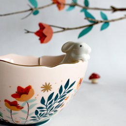 A decorative ceramic bowl with a rabbit figurine, featuring a floral pattern in vibrant colors including red, green, and white.