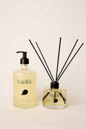  Luxe reed diffuser set with earthy, woodsy scent. Features amber-colored glass bottle and black reed sticks.
