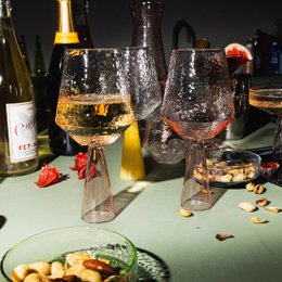 Two pink-tinted wine glasses with a bottle of wine in the background. The glasses have a unique textured design.