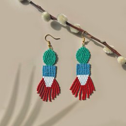  Handmade, beaded earrings in a statement style with a vibrant color palette of red, orange, and blue. The earrings feature a round bead at the top and long, tassel-like strands hanging below.