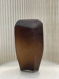 A tall, brown glass vase with a unique, angular shape. The vase features a rich, chocolate-brown color and a sleek, modern design that would complement a variety of home decor styles.