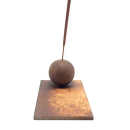 Rustic industrial incense holder with a round, rusty metal sphere on a square cork base.