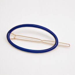 Oval-shaped hair clip in various colors including Blanc, Nude, Brique, Ambre, Mousse, Midnight Blue, Sans Email, Prusse, Corail, Aniline, Sable, and Massaï. The clip features a simple, minimalist design with a metal frame and a soft, textured surface.