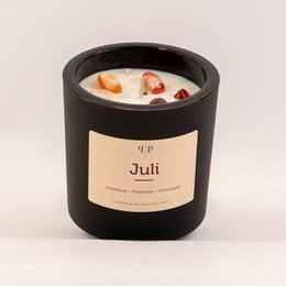 Gemstone scented candle in a black container with a label that says "Juli". The candle has a round, tall shape and appears to be made of wax with visible gemstones or crystals embedded in it.