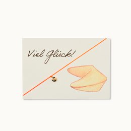  "Good luck card with fortune cookie-shaped bracelet. Beige and orange color scheme, featuring a fortune cookie-shaped bracelet and a 'Viel Glück!' (Good Luck in German) message."