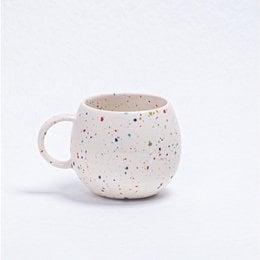 A round, white ceramic mug with a speckled pattern of colorful dots, suitable for parties and casual use.