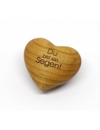 Wooden heart-shaped ornament with the text "Du bist ein Segen!" (German for "You are a blessing!") carved into the surface. The ornament has a natural, rustic appearance and is placed on a wooden surface with bark.