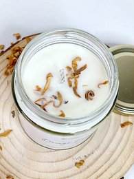 Tall, round, white candle with orange blossom scent and dried flower petals visible inside the glass jar.