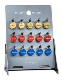 Assorted key fobs in various colors and shapes, including round, oval, and heart-shaped designs. The key fobs feature text such as "Courage" and "Strength" printed on them.