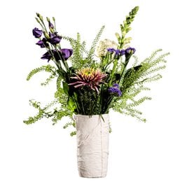 Tall, cylindrical white ceramic vase with a textured, crinkled surface and a wide opening at the top. The vase contains a vibrant floral arrangement featuring purple irises, green ferns, and other greenery.