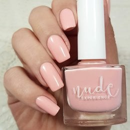 A light pink nail polish bottle with a white cap, displayed on a textured surface.