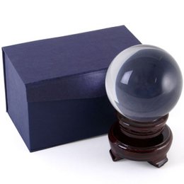 A clear glass crystal ball with a wooden base, encased in a navy blue box. The crystal ball has a smooth, spherical shape and a polished finish, sitting atop a dark wooden stand.