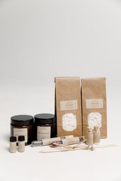 DIY candle making kit with essential oils, flowers, and other craft supplies in a cardboard box.