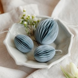Light blue paper Easter eggs in a white ceramic dish with small white flowers.